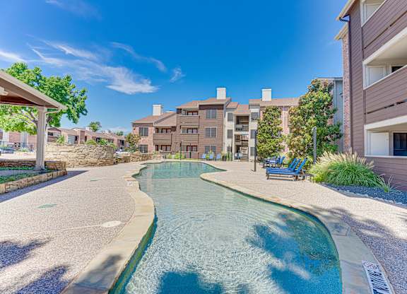 A swimming pool in a residential area surrounded by buildings and trees. at Timberglen Apartments, Dallas