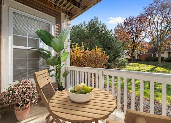 A wooden chair sits on a porch with a bowl of fruit on the table.