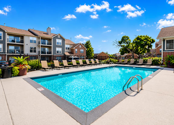 A swimming pool surrounded by a concrete patio and lounge chairs.