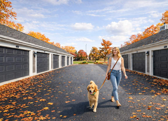A woman walking her dog on a street lined with garages.