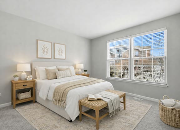 A bedroom with a large bed, a nightstand, a small table, and a window with a view of a building outside.