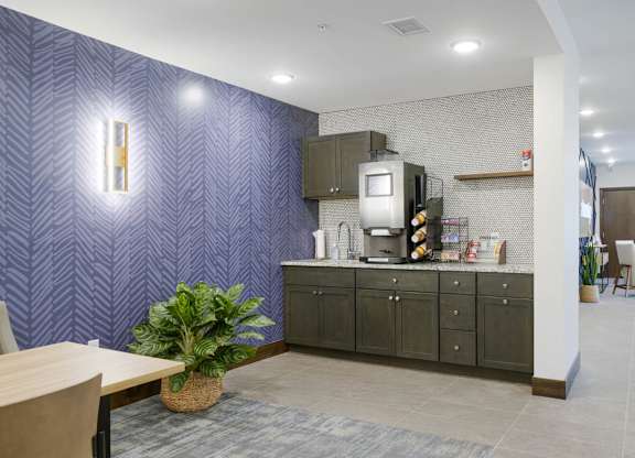 Resident coffee bar with dark cabinetry, countertop coffee machine, and open shelving, accented by patterned wallpaper, tile backsplash, and adjacent lounge seating area.