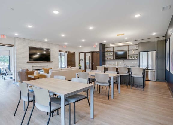 a community room with a kitchen, tables and chairs, and seating in front of a tv and fireplace