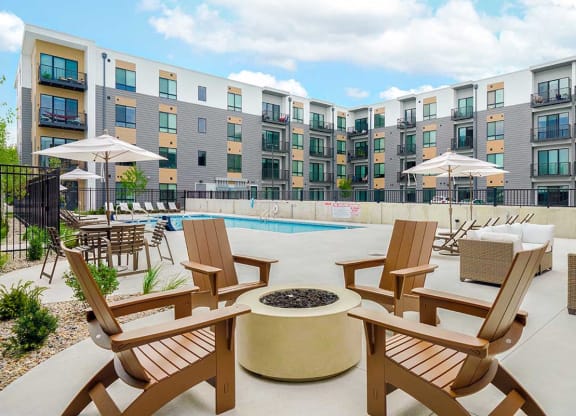 a firepit in front of a pool with chairs and umbrellas in front of an apartment building
