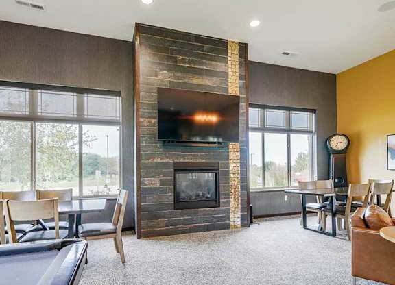 A modern TV lounge with a tiled fireplace, mounted TV, and several seating options.