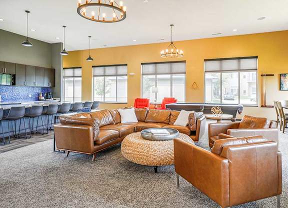 A clubhouse TV lounge with brown leather couches and chairs.