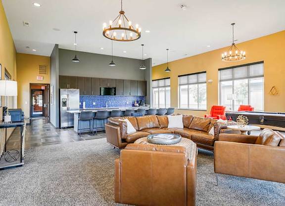 A clubhouse kitchen with large island and several bar stools, and a lounge area with a leather couch, chairs, and a pool table.