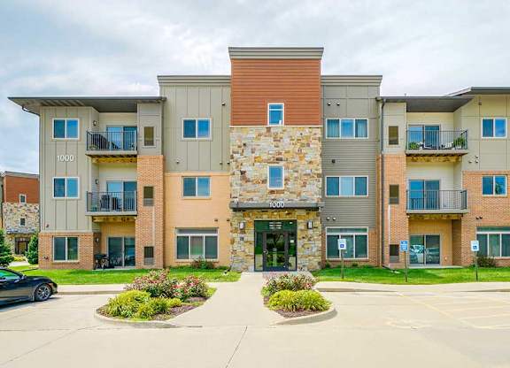 A modern stone and brick apartment building with several balconies and patios, and a front door with controlled-access entry.