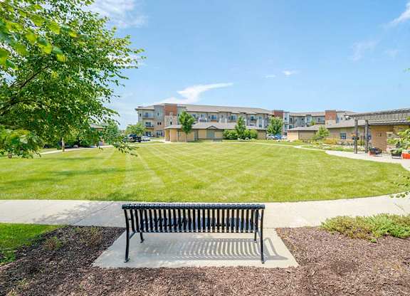 An expansive green courtyard lawn with a walking path around the edge, and a bench to rest on.