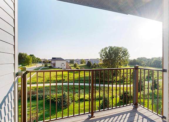 A balcony with a view of a green space, with houses in the distance.