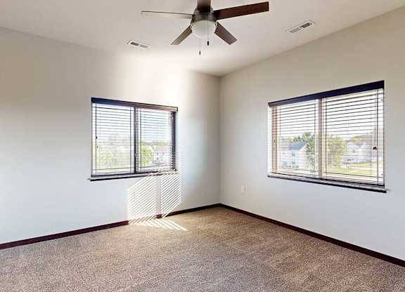 A bedroom with a ceiling fan, and two windows - one on each wall.