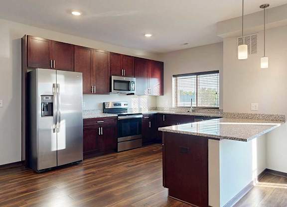 A modern kitchen with dark wooden cabinets, granite countertops, stainless steel appliances, a large window over the sink, and a peninsula counter.