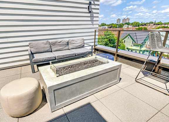 A grey couch and ottoman are on a patio with a fireplace.