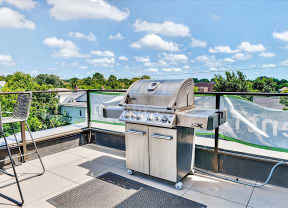 A BBQ grill is on a balcony with a view of trees and houses.