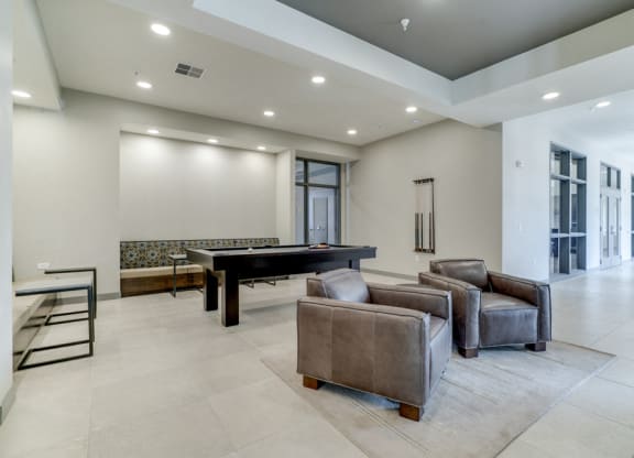 Game room in Ascend at Woodbury apartments' clubhouse with pool table and leather chairs.
