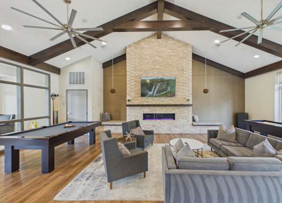 Spacious apartment community clubhouse with vaulted wood-beam ceilings, stone fireplace, lounge seating, and pool table.