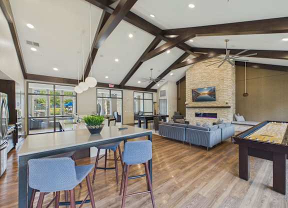 Bright apartment community clubhouse with vaulted wood-beam ceilings, lounge seating, dining tables, and large windows.