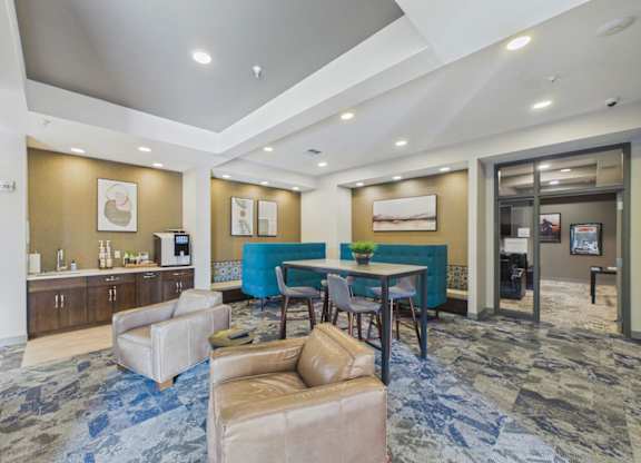 Apartment community lounge with teal seating, café tables, soft seating, patterned carpet, and recessed lighting.