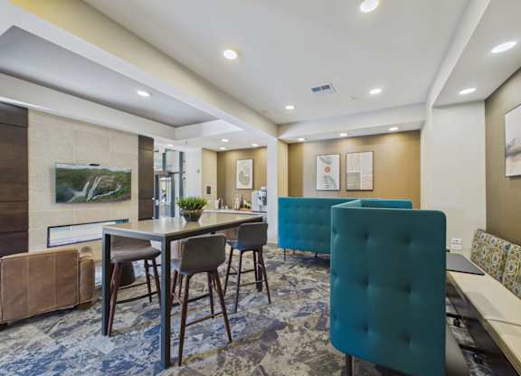 Modern apartment community lounge with teal seating, a high-top table, wall-mounted TV, and recessed lighting