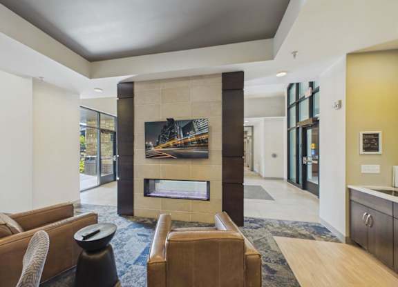 Apartment community lounge with leather seating, a wall-mounted TV, modern fireplace, tray ceiling, and adjacent coffee station.