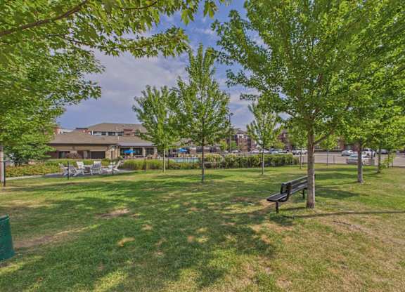 Landscaped apartment community courtyard with mature trees, grassy lawn, walking paths, and outdoor benches.