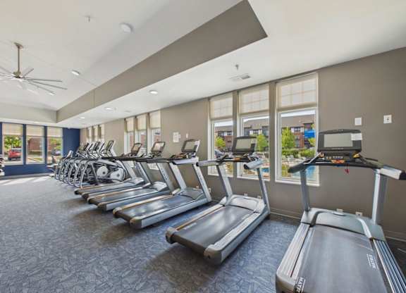 Apartment community fitness center with rows of treadmills and cardio equipment, large windows, and bright overhead lighting.