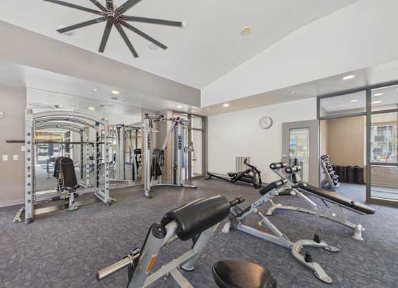 Apartment community fitness center with weight-training machines, cardio equipment, rubber flooring, and a large ceiling fan.