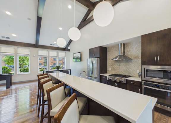 Apartment community kitchen with a large island, bar seating, dark wood cabinetry, pendant lights, and stainless steel appliances.
