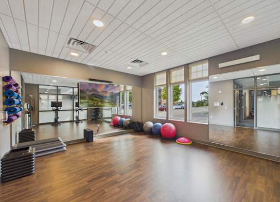 Bright apartment community fitness studio with wood flooring, mirrored walls, exercise balls, and large windows.