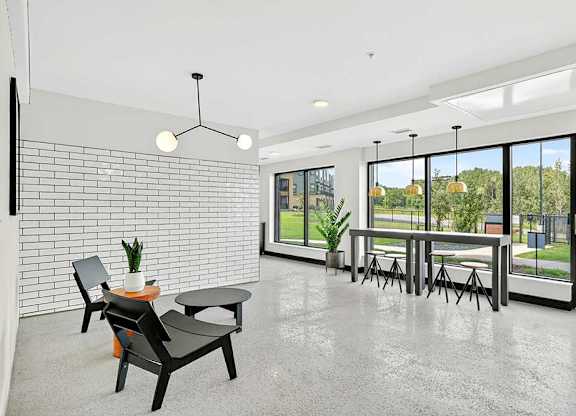 Bright apartment community lounge with polished concrete floors, modern seating, white tile accent wall, and large windows with views of green outdoor space.