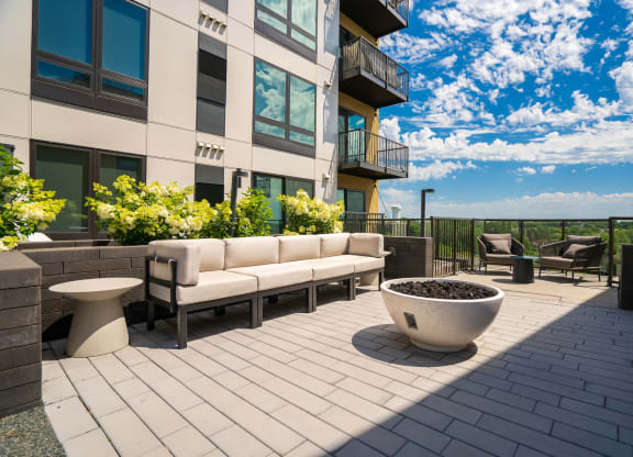 Outdoor lounging area with beige couch, a couple chairs, and fire place.