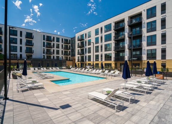 Resort style swimming pool with white sun loungers and green circular side tables at Aspire at CityPlace