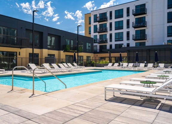 Resort style swimming pool with white sun loungers and green circular side tables at Aspire at CityPlace