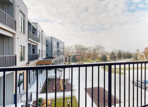 a balcony with a black railing overlooks a parking lot and apartment buildings