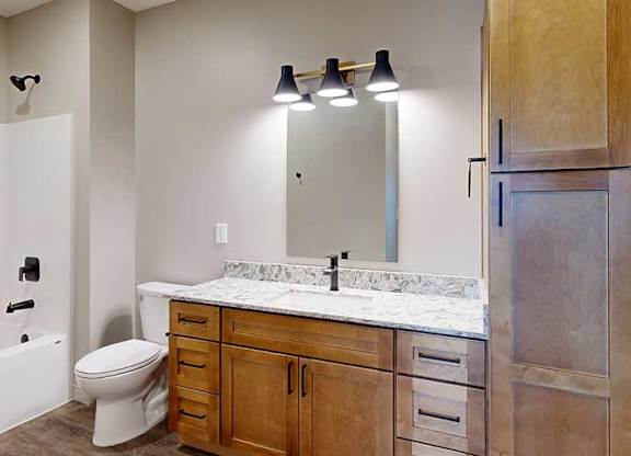 a bathroom with a light brown cabinets, a tall storage cabinet, quartz vanity sink, a mirror, and a shower and tub