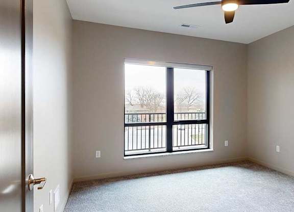 a bedroom with a ceiling fan and a large window overlooking a balcony