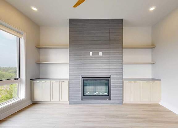A modern living room with a fire place in a floor-to-ceiling mantel, and built-in cabinetry and shelves on either side.