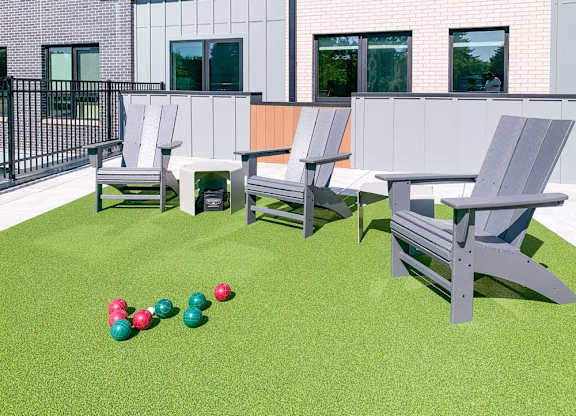 a set of bocce balls in front of Adirondack chairs on a green turf