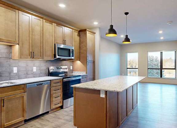 a kitchen with a large central island featuring tan wooden cabinets and light quartz countertops
