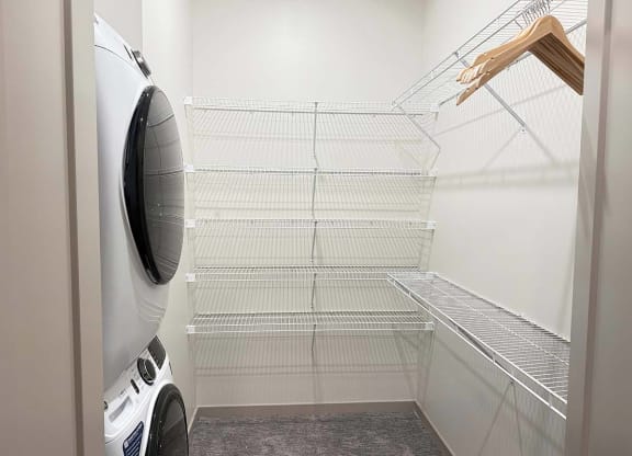a walk-in closet with built-in shelving and hanging space and a stackable washer and dryer in it