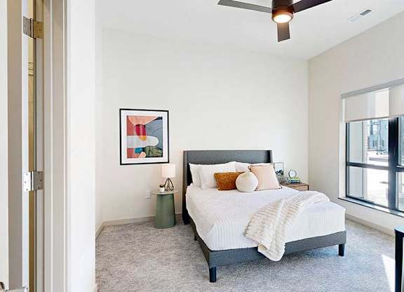 a view of the bedroom from the doorway, furnished with modern decor, a ceiling fan, and a large window overlooking the courtyard