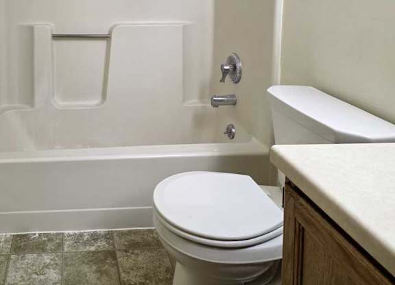 A bathroom with a sink, and a white tub shower with chrome finishes.