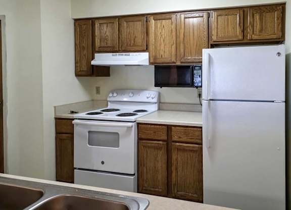 A kitchen with wooden cabinets, white appliances, and a mounted microwave.