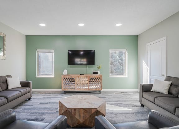 a tv lounge space with a pale green wall, tv stand, and couches