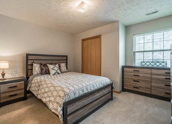 A bedroom with a large bed, a nightstand with a lamp, and a nook with a large window