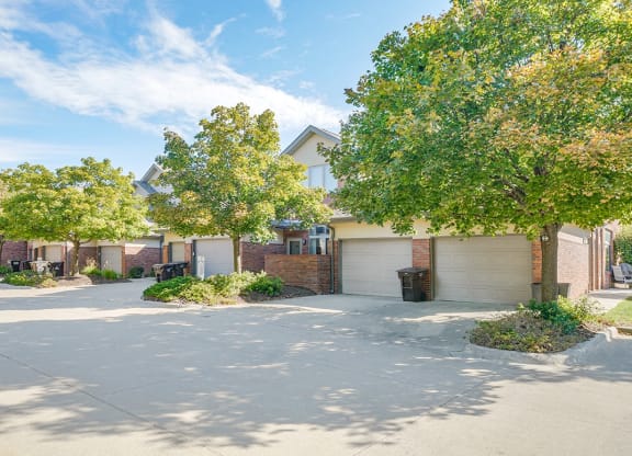 the exteriors of a row of villas with attached garages and trees lining the road