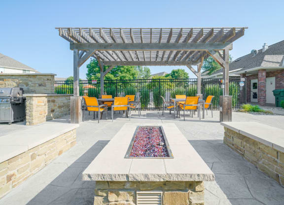 a patio with a fire pit and two stone benches and a pergola
