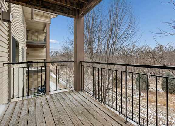 Private apartment balcony with wood decking, metal railing, and views of mature trees, offering an outdoor space accessible from the apartment.