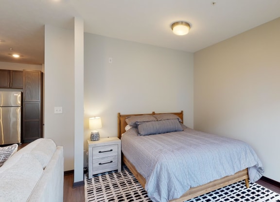 a studio with a bed and bedside table with lamp