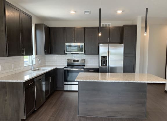 Large kitchen with warm dark brown cabinets, stainless steel appliances, and an island
